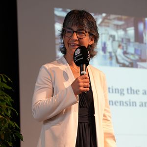 Frau mit Mikrofon vor großer Leinwand 