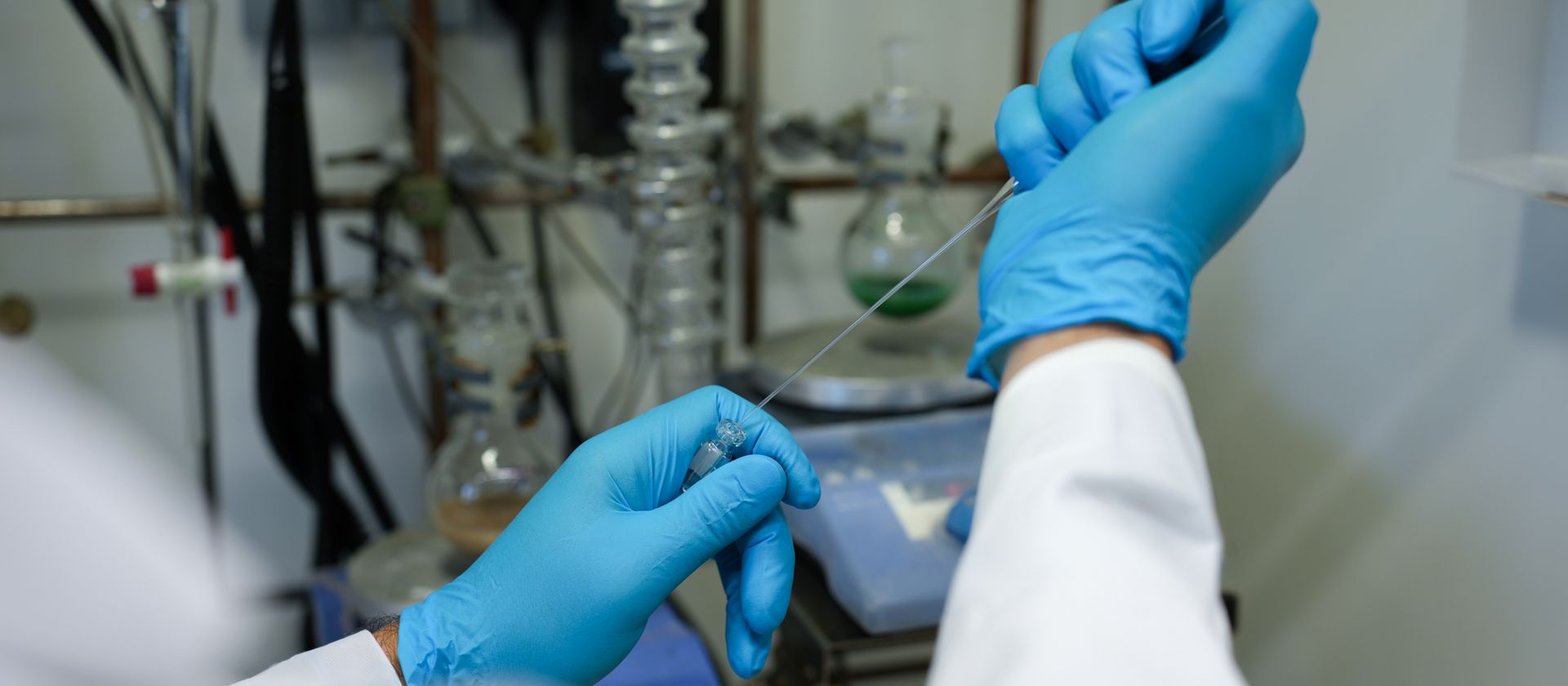 Einblick in ein Labor; zwei Hände mit blauen Handschuhen die mit einer Pipette arbeiten