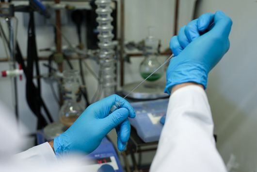 A view inside a laboratory; two hands wearing blue gloves working with a pipette
