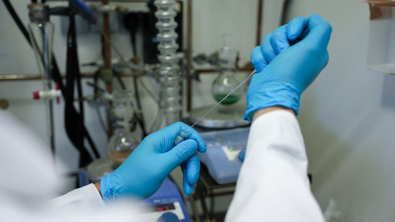  A view inside a laboratory; two hands wearing blue gloves working with a pipette