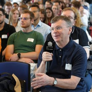 Mann im Publikum sitzend mit Mikrofon in der Hand 