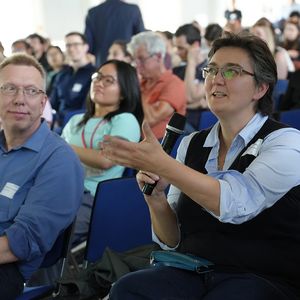 A person holding a microphone, surrounded by people sitting in chairs