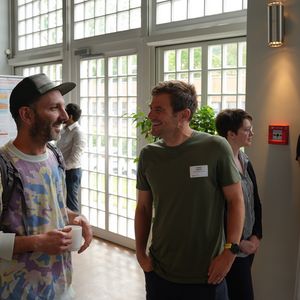 Zwei Männer lachend, in einem Raum mit wissenschaftlichen Postern auf Trennwänden 