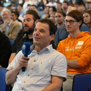 Mann im Publikum sitzend mit Mikrofon in der Hand 