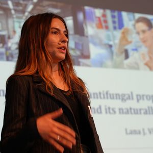 Frau mit Mikrofon vor großer Leinwand sprechend 