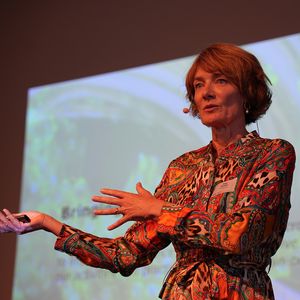 Frau mit Mikrofon hält eine Rede vor großer Leinwand 