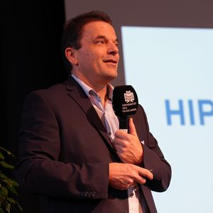 Mann mit Mikrofon vor großer Leinwand 