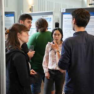 Vier Personen unterhalten sich zwischen wissenschaftlichen Postern auf Trennwänden 